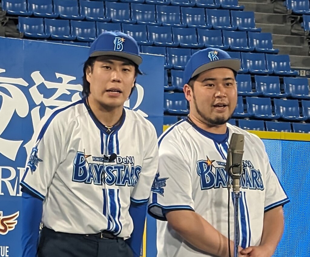 横浜DeNAベイスターズの選手たちが白と青のユニフォームを着て青い座席席の前に立っている試合会場の様子
